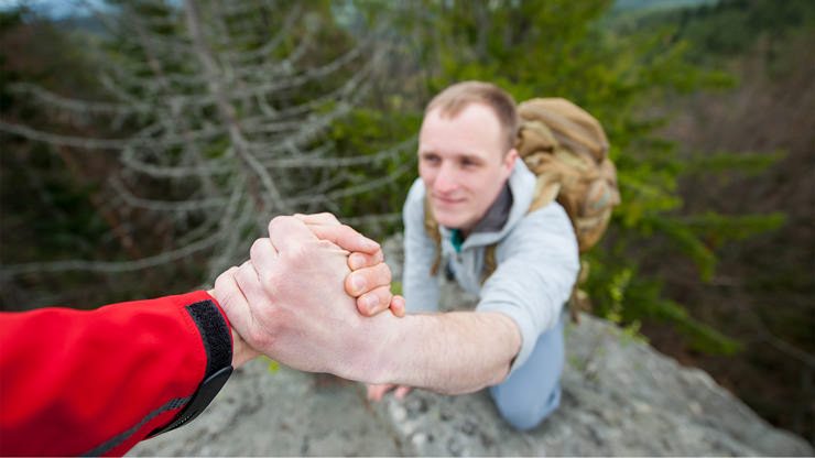 man helping hiker up cliff