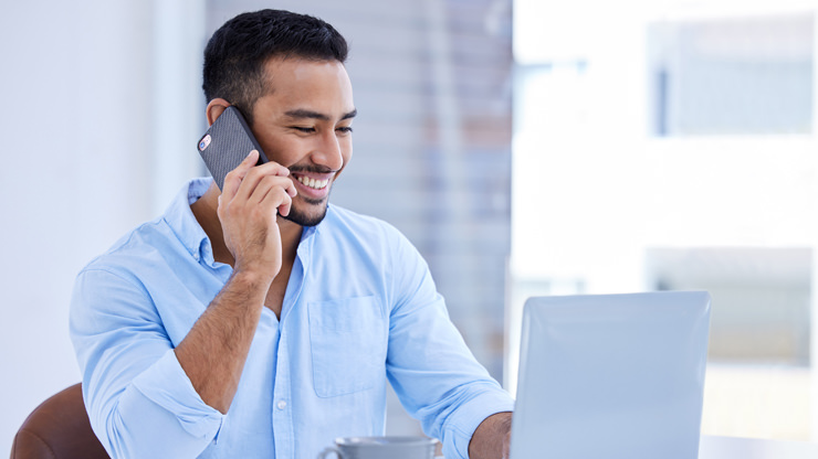 young man on telephone sitting at desk with laptop computer